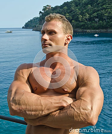 Attractive muscular young man outside in front of the sea, arms crossed