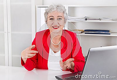 Attractive older smiling senior businesswoman sitting at desk we