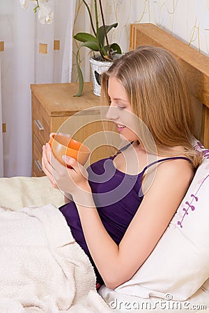 Attractive woman sitting in bed with mug of coffee or tea