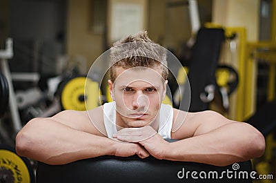 Attractive young athletic man resting on gym equipment