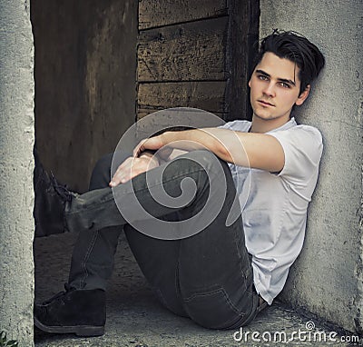 Attractive young man sitting on old door s threshold