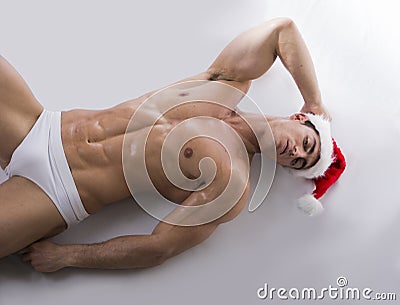 Attractive young muscle man on the floor in Santa Claus s red hat