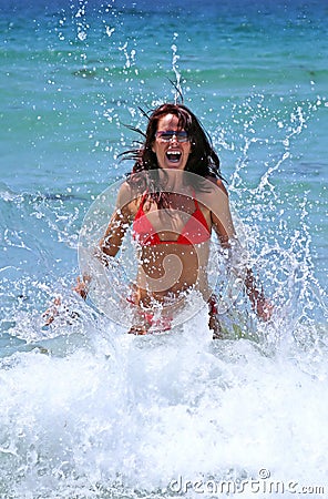 Attractive young woman in red bikini being splashed by a cold crystal blue wave on the beach