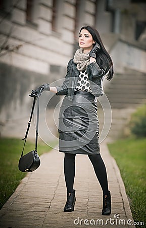 Attractive young woman in a winter fashion shot. Beautiful fashionable young girl in black leather waking on avenue. Elegant woman