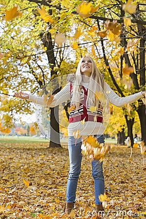 Autumn leaves falling on young woman with arms outstretched in park