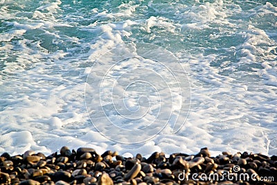 Azure sea waves. Clear blue water with white foam. Pebbles on th