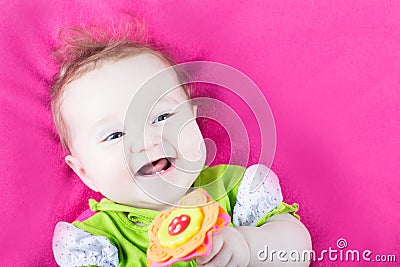 Baby girl playing with her toy flower on a pink blanket