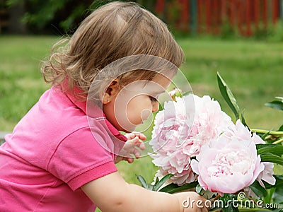 Baby girl smelling peony flowers