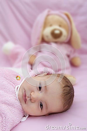 Baby lies on pink toy bear background