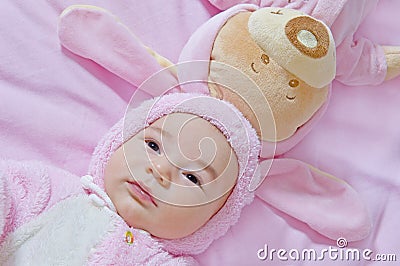 Baby lies with toy bear in pink costumes