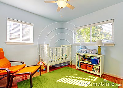 Baby nursery room design with green rug, blue walls and orange chair.