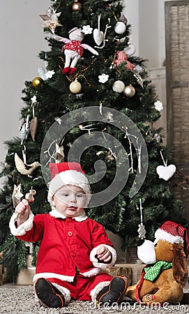 Baby in Santa costume sit near decorating Christmas tree with toy