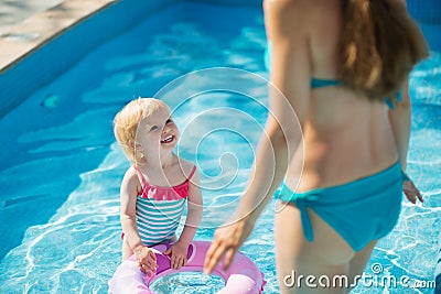 Baby standing in pool and looking on mother