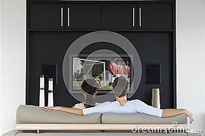 Back view of couple watching soccer game on television in living room