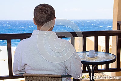 Back view of man sitting on balcony with sea view