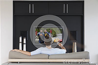 Back view of mid-adult man changing channels with television remote control in living room
