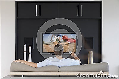 Back view of mid-adult man changing channels with television remote control in living room