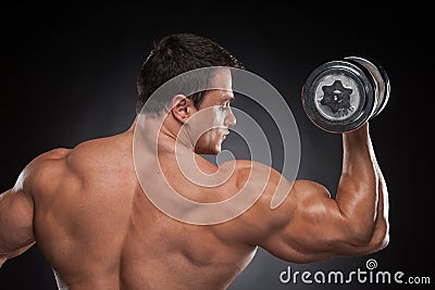 Back view muscular man lifting dumbbell up.
