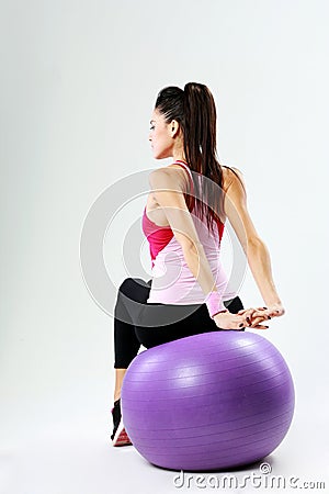 Back view of a young sport woman stretching on fitball