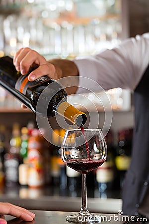 Red wine pouring in glass at bar