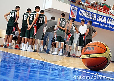 Basketball ball pictured with a team gathered around coach in background