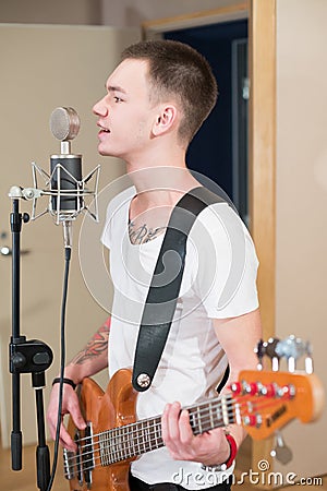 Young bass player with tattoo standing with his guitar and singing 