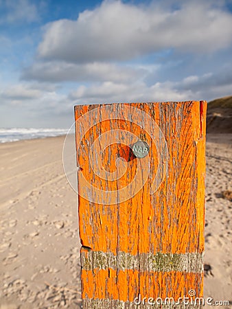 Beach post with sea level marker with beach and sea behind