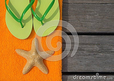 Beach slippers, towel and starfish on wood background