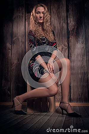 Beautiful blond curly hair model sitting in a pose on the box over wooden wall background
