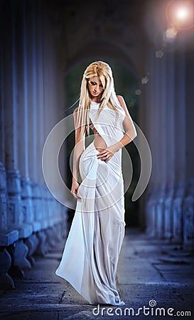 Beautiful blonde angel with white light wings and white veil posing outdoor