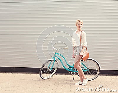 Beautiful blonde girl is standing near the vintage bicycle with brown vintage bag, warm, tonning