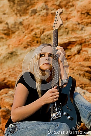 Beautiful blonde with a guitar on rock background