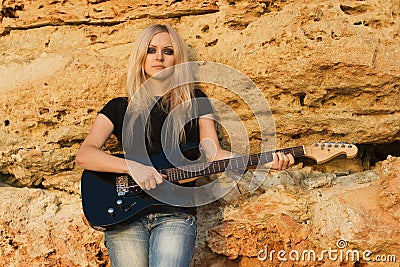 Beautiful blonde with a guitar on rock background