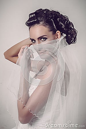 Beautiful brunette bride holding veil over her smiling face