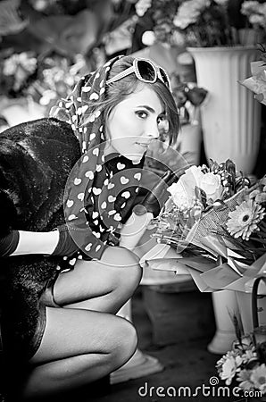 Beautiful brunette woman with gloves choosing flowers at the florist shop. Fashionable female with sunglasses and head scarf