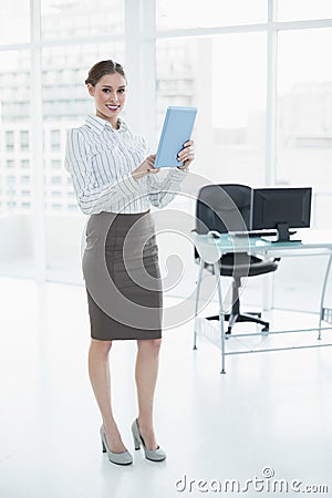 Beautiful calm businesswoman holding her tablet standing in her office