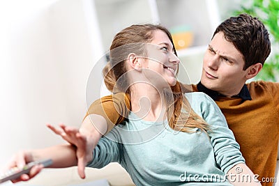 Beautiful couple bickering to change tv channel on remote contro