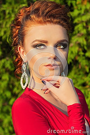 Beautiful elegant girl with beautiful makeup and hair in a red evening dress in the Park