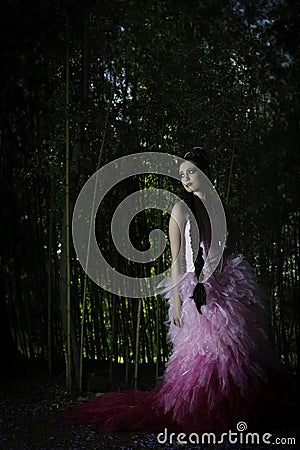 Beautiful fantasy woman in pink evening dress standing in enchanted forest looking back over her shoulder