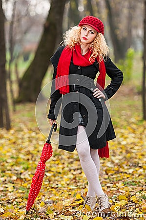 Beautiful fashionable young girl with red umbrella , red cap and red scarf in the park