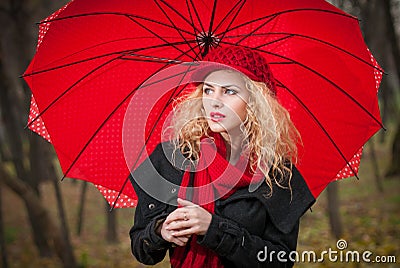Beautiful fashionable young girl with red umbrella , red cap and red scarf in the park