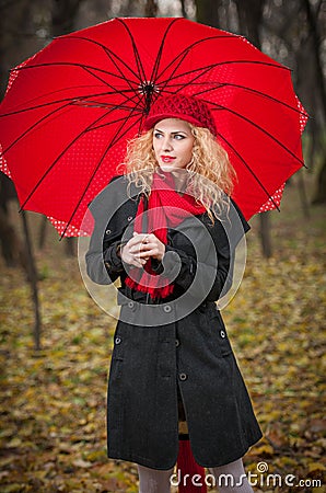 Beautiful fashionable young girl with red umbrella , red cap and red scarf in the park