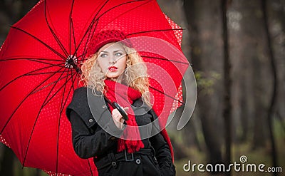 Beautiful fashionable young girl with red umbrella , red cap and red scarf in the park