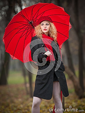 Beautiful fashionable young girl with red umbrella , red cap and red scarf in the park