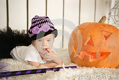 Beautiful girl with Down syndrome thoughtfully keeps finger in the mouth near the big pumpkin