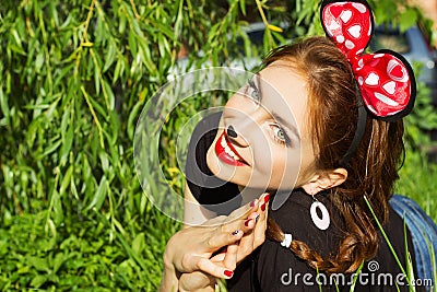 Beautiful girl happy smiling in the costume of a mouse with a big red bow down on the grass in the Park