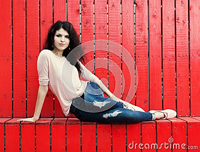 Beautiful girl with long hair brunette in jeans sits near wall of red wooden planks