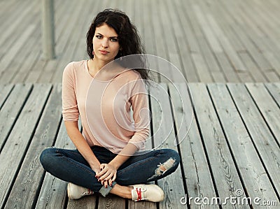 Beautiful girl with long hair brunette in jeans sits on wooden planks