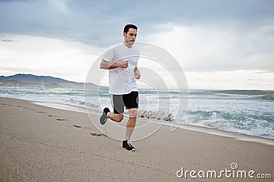 Beautiful male athlete runs along the beach along the sea, mountain beach background