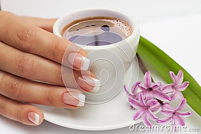 Beautiful manicured hand with french nails and cup of coffee and flowers at saucer